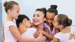 girls in ballet costumes hugging a teacher and smiling